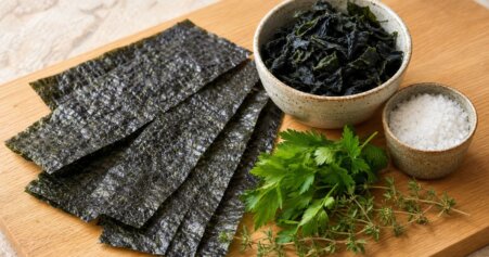 Stillleben mit jodreichen Lebensmitteln: Nori-Blätter, Wakame-Algen und Meersalz als vegane Jodquellen auf Holzuntergrund.