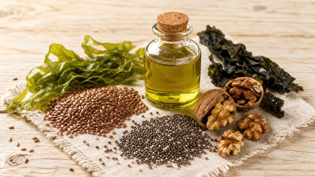 Stillleben mit pflanzlichen Omega-3-Quellen: Leinsamen, Chiasamen, Walnüsse und eine Glasflasche mit Algenöl auf hellem Holzuntergrund.